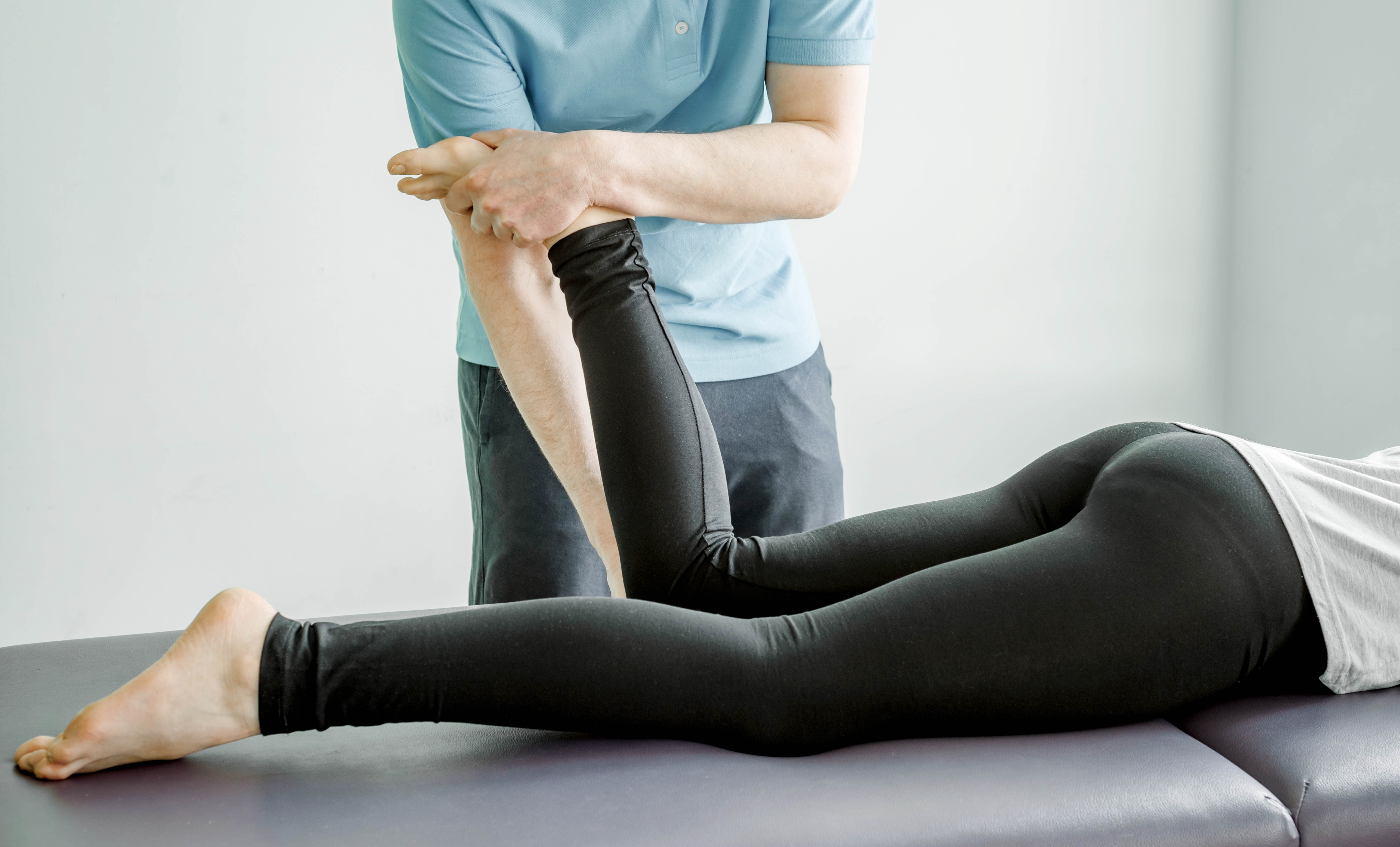 Young female patient lays face down on the table, practitioner is doing fascial stretch therapy on her lower leg and knee